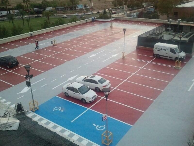 Aparcamiento en cubierta con pavimento de poliurea señalizado en rojo, gris y azul, con plazas de movilidad reducida y tráfico rodado en servicio